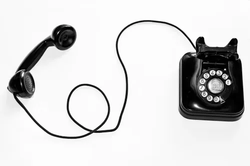 A black rotary telephone with its handset off the hook