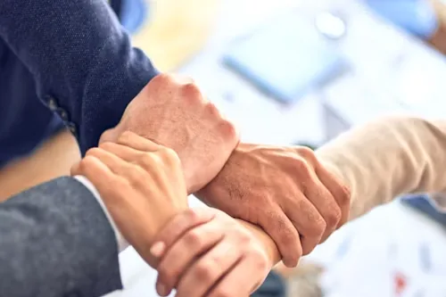 Three people gripping each other's wrists in a linked square over a desk