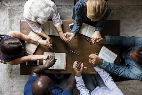 A group sitting around a table with their hands joined over open books