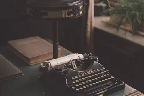 A vintage typewriter on a wooden desk beside a lamp and old books