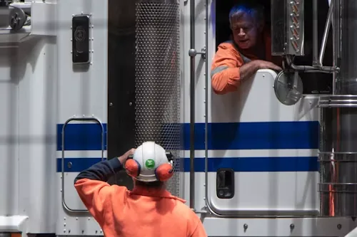 A driver leaning from his cab window talking with a worker on the ground