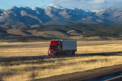 A tractor-trailer on an open highway with mountains behind