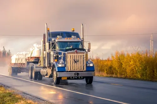 An owner-operator's rig on a wet highway at dawn